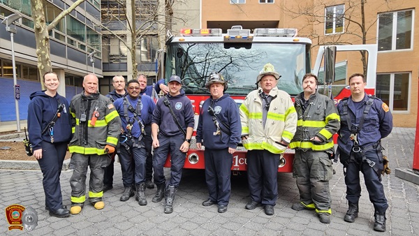 Firefighter rescuers standing in front of Rescue 1's apparatus, with a high-rise building in the background, after rescuing 2 trapped people.