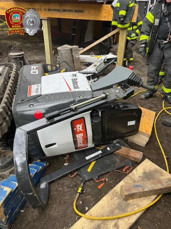 Firefighters work to rescue a person who was trapped under an excavator at a construction site