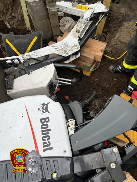 Firefighters in full PPE working to extricate a person who was trapped under an excavator