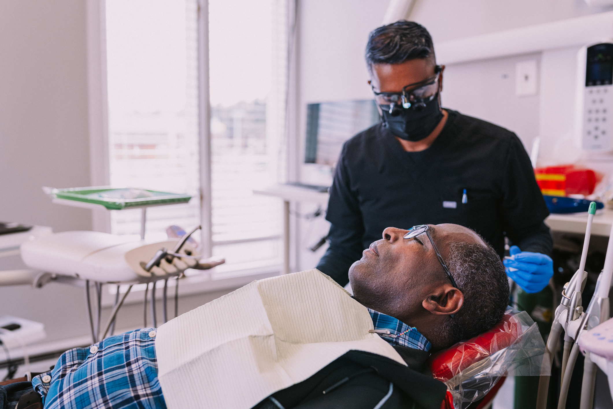 A mature adult Black man lies in a dentist's chair as his dentist prepares to clean his teeth during a routine appointment.