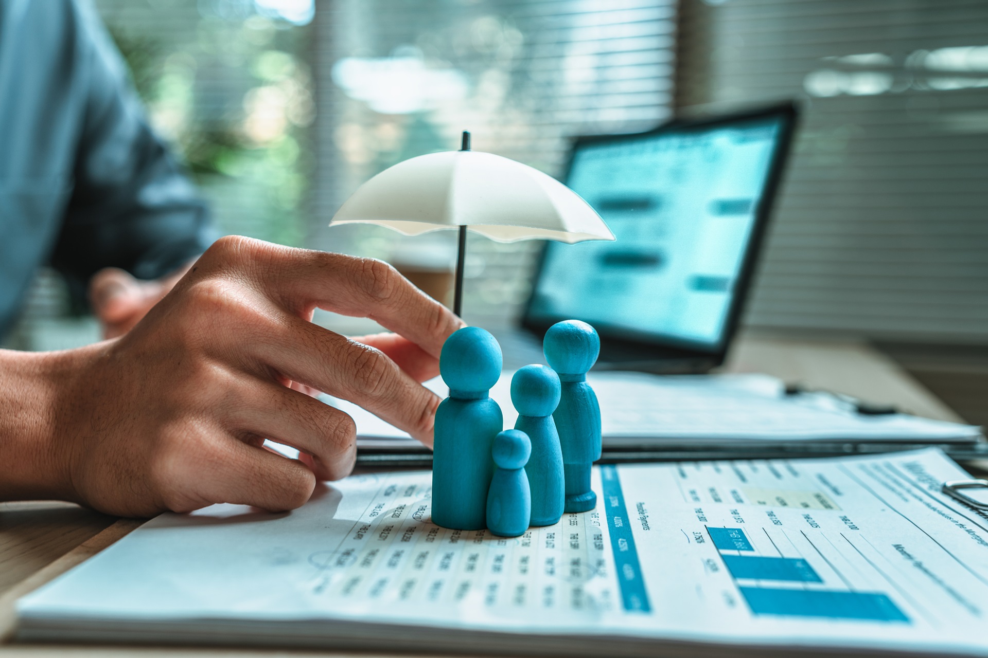 Three blue wooden dolls sit on a piece of paper as a man holds a small umbrella over them