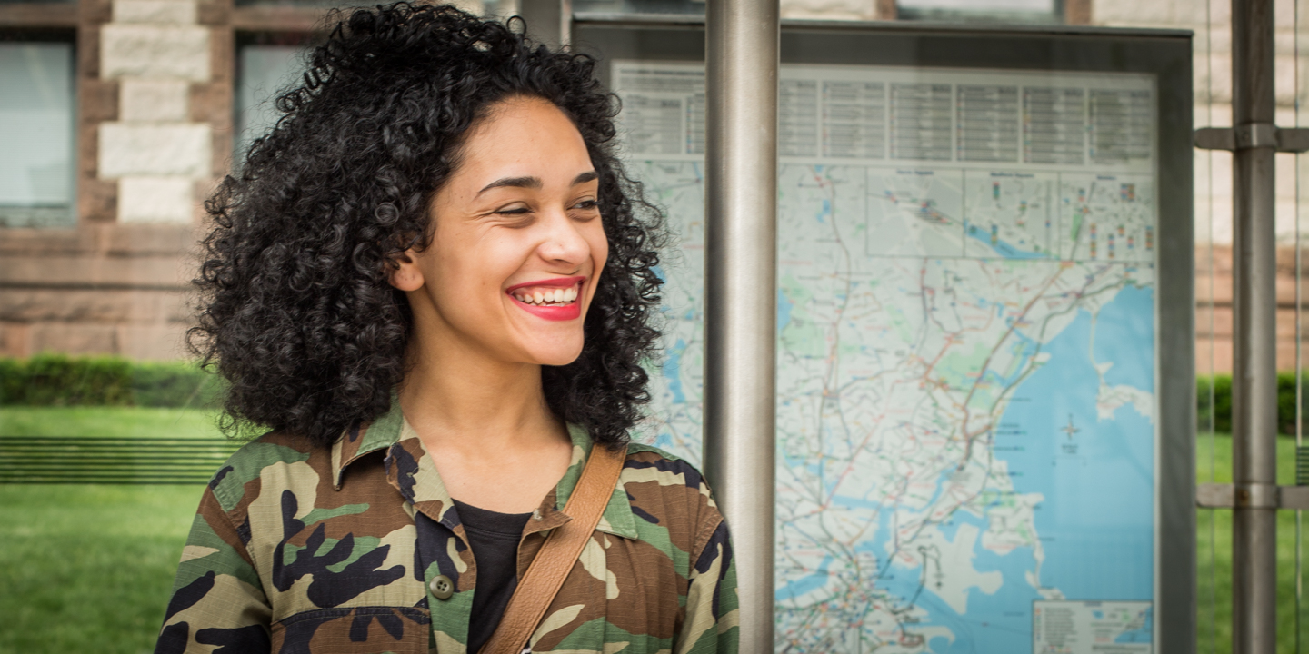 A young woman standing at a bus stop is smiling
