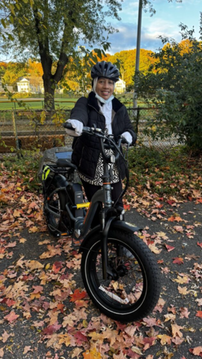 A woman wearing a helmet while standing next to an electric bicycle that she purchased through the City's bike voucher program