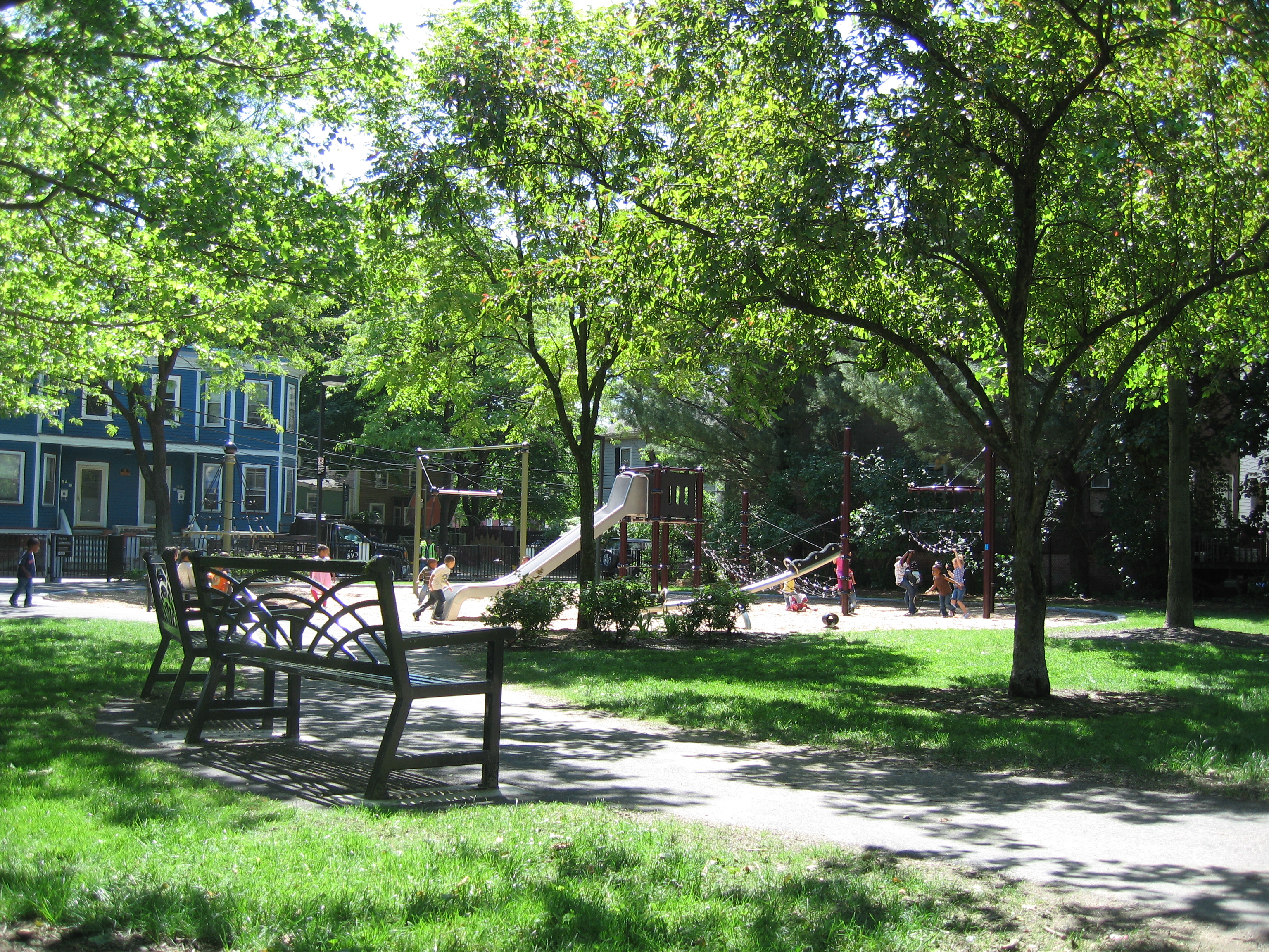 Park benches in the foreground, children playing at a playground in the background