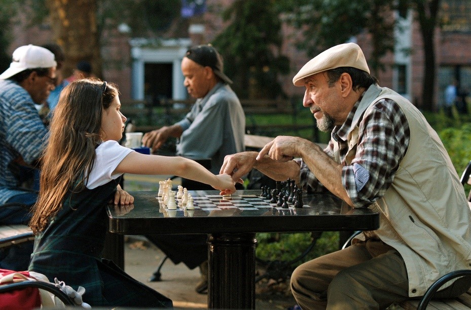 A still from the movie A Little Game showing a man and a child playing chess together in a park