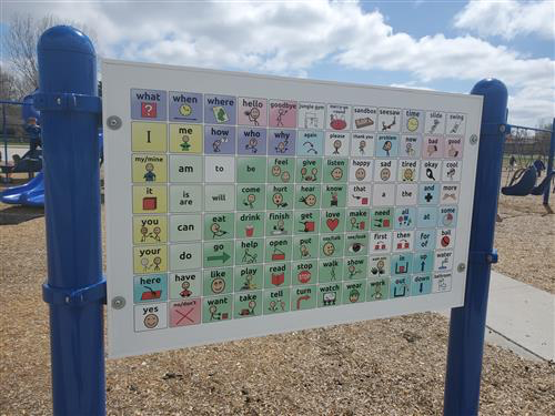 A large sign in a playground with squares depicting common English words, such as "hello" and "happy," along with pictures representing the words.