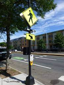 A sign at a crosswalk with flashing lights to warn drivers that a pedestrian is trying to cross.