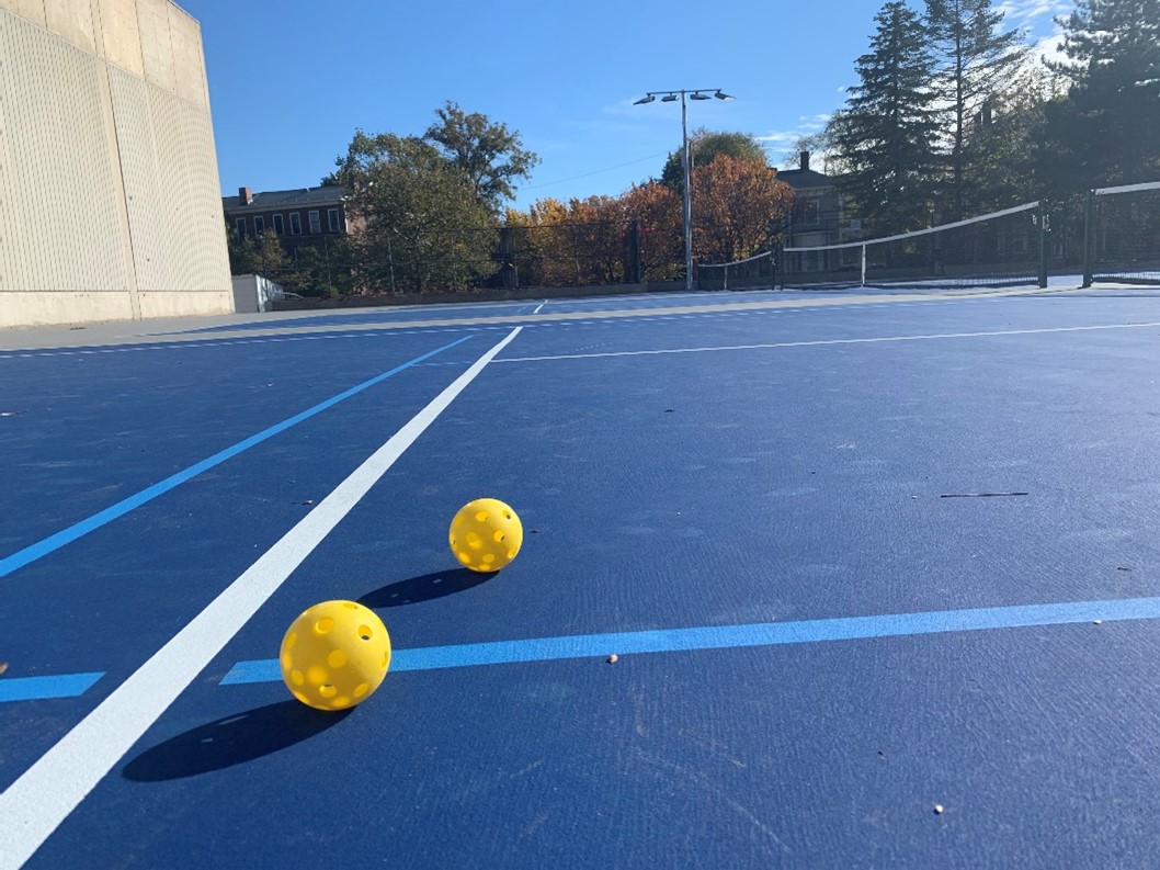 Two pickleballs in the corner of a pickleball court with the net on the right side.