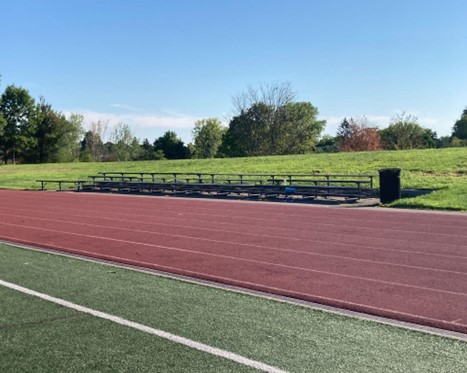 A portion of a track.  Next to the track are bleachers, with a row of trees behind them.