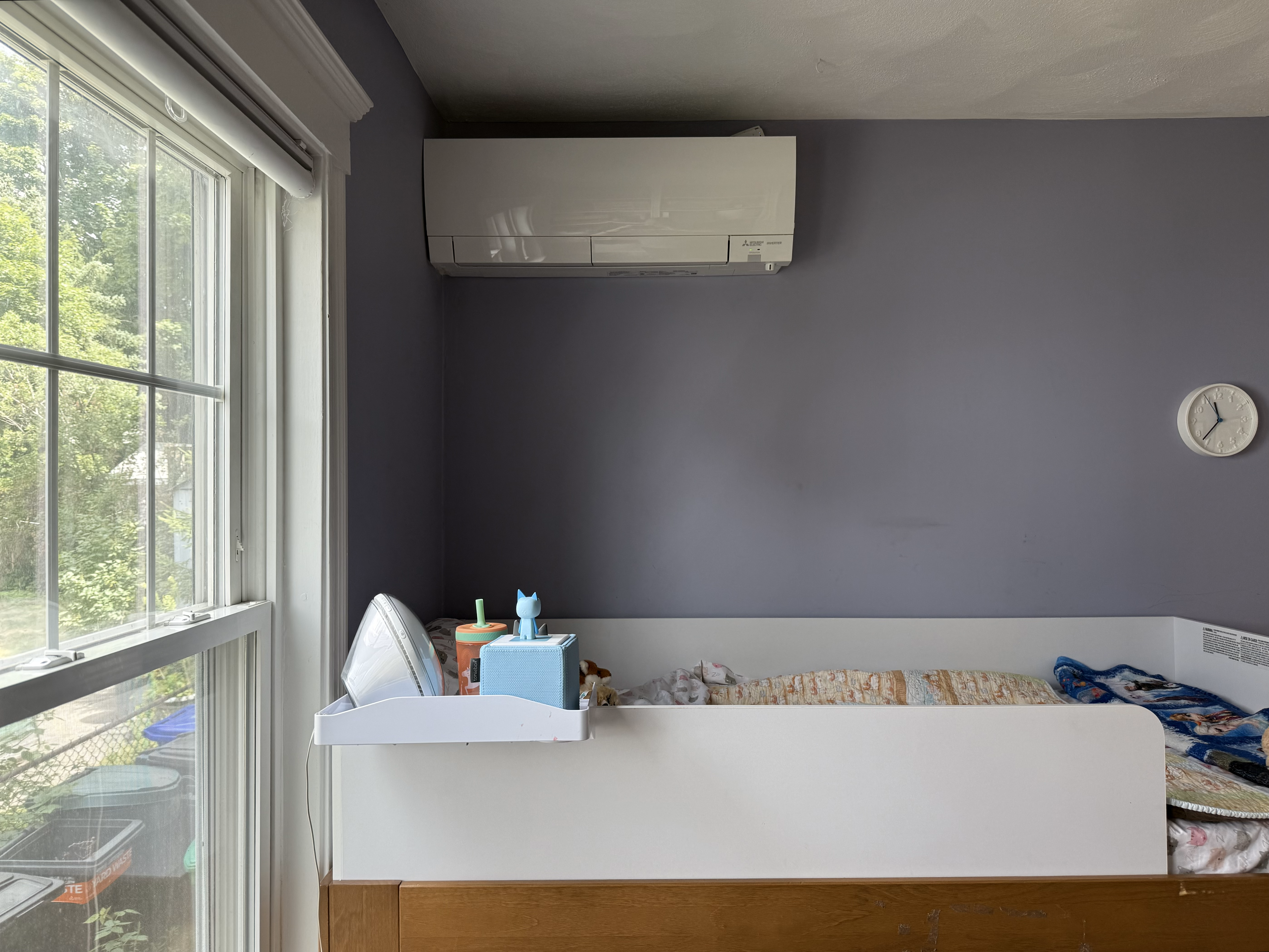 A picture of a child's bedroom with a white heating pump unit near the ceiling. 
