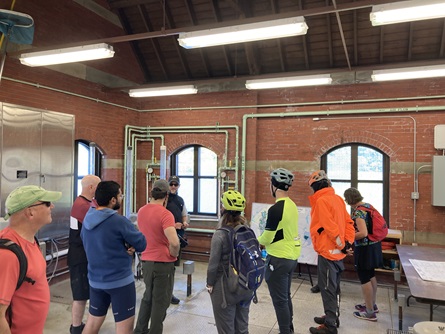 Watershed staff talk to bike riders inside the Stony Brook Gatehouse. Red brick walls and mechanical equipment surround everyone.