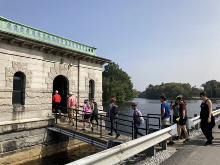 People walk across a bridge from a road into the Hobbs Brook Reservoir Gatehouse.