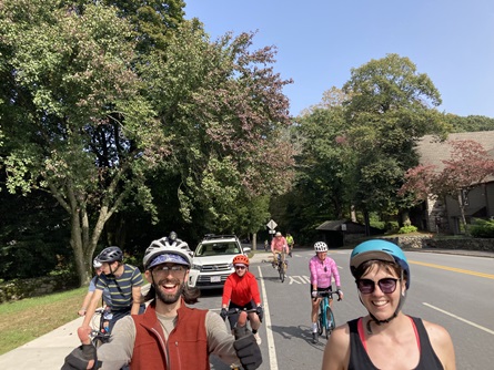 Participants on bikes smile for the camera as more people gather behind them at a stop sign.