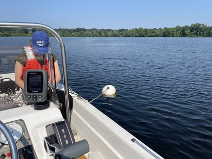 A person collects water quality probe readings from a boat on Fresh Pond Reservoir