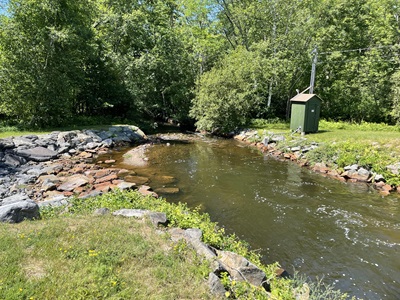 A green USGS monitoring station shed next to a tributary in the Cambridge watershed