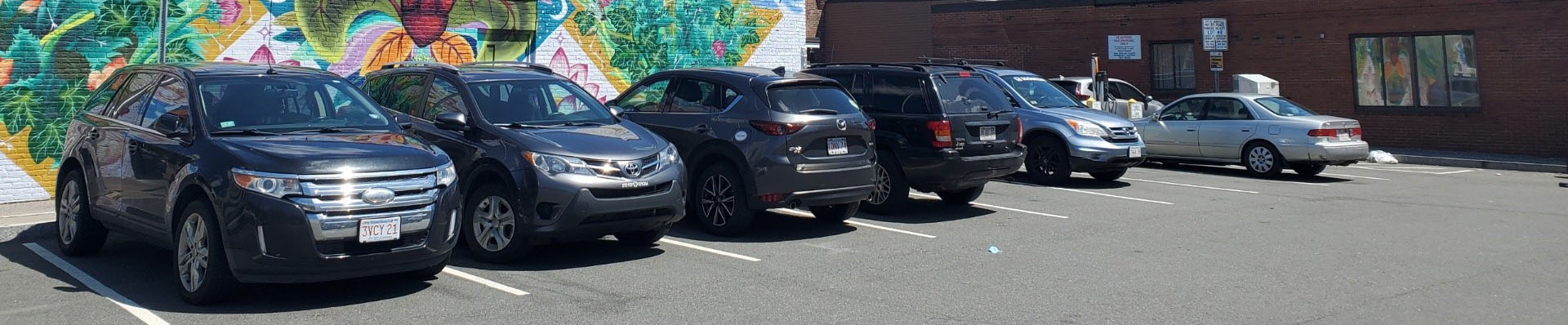 Row of parked cars in a lot with a colorful mural behind