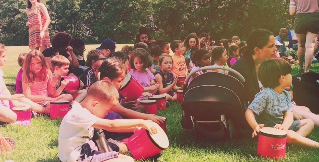 Children play bongo drums outdoors during a 2016 Summer in the City performance in Cambridge