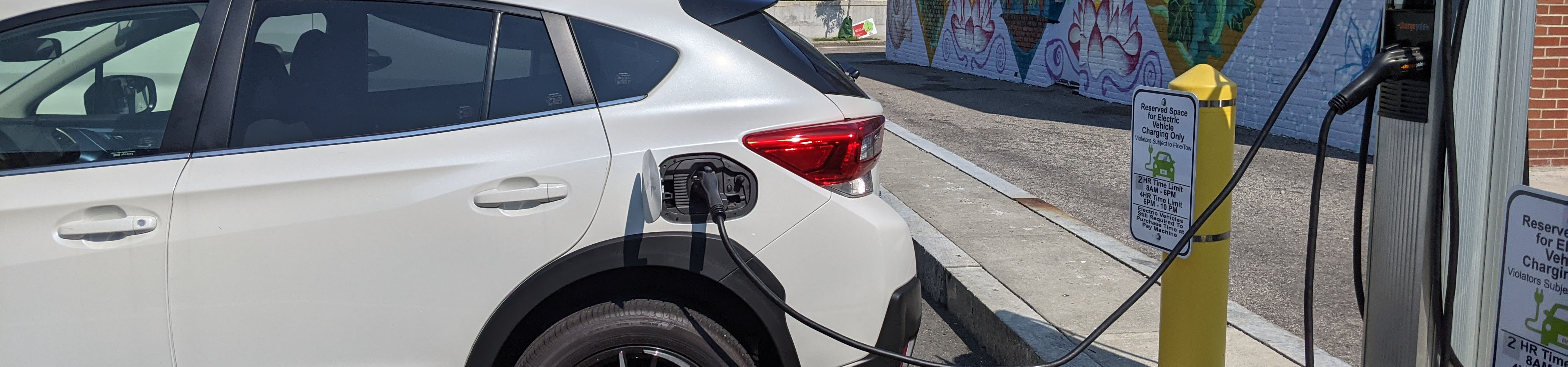 A white hatchback plugged into an EV charger in an outdoor parking lot