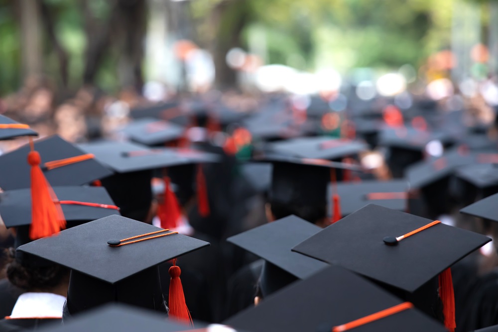 Close-up of multiple graduation caps with orange tassels during an outdoor ceremony.