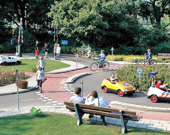 Park with a traffic garden, children playing in toy cars while parents watch
