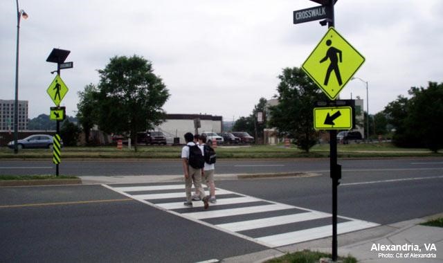 Two people in the middle of a crosswalk with a pedestrian crossing sign in foreground