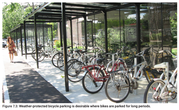 More than a dozen bikes parked at a series of three bike corrals under overhangs.