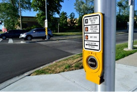 A button affixed to a walk signal at an intersection that turns on audio explanation of when it is safe to cross the street.