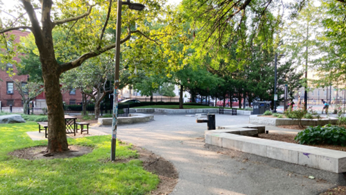 A path leading through a park, with tables, seating areas, and a water fountain.