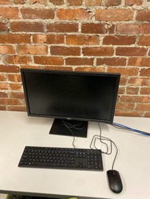 A computer on a table in front of a brick wall.